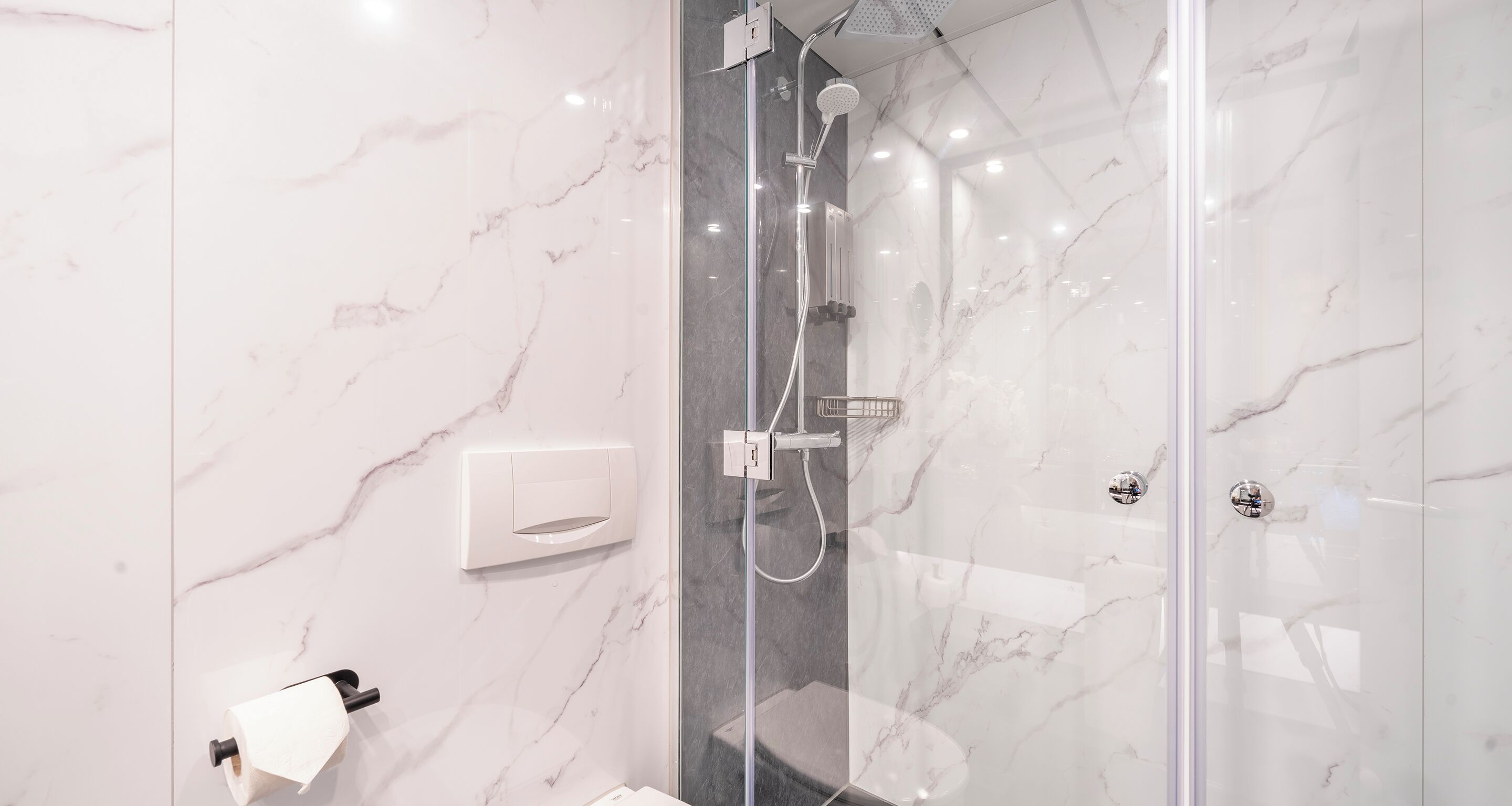 Une salle de bain moderne avec une douche à parois de verre, des murs en marbre et un porte-rouleau de papier toilette.
