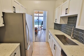 Una cocina con armarios blancos, un refrigerador de acero inoxidable, salpicadero de azulejos y vista a un balcón.