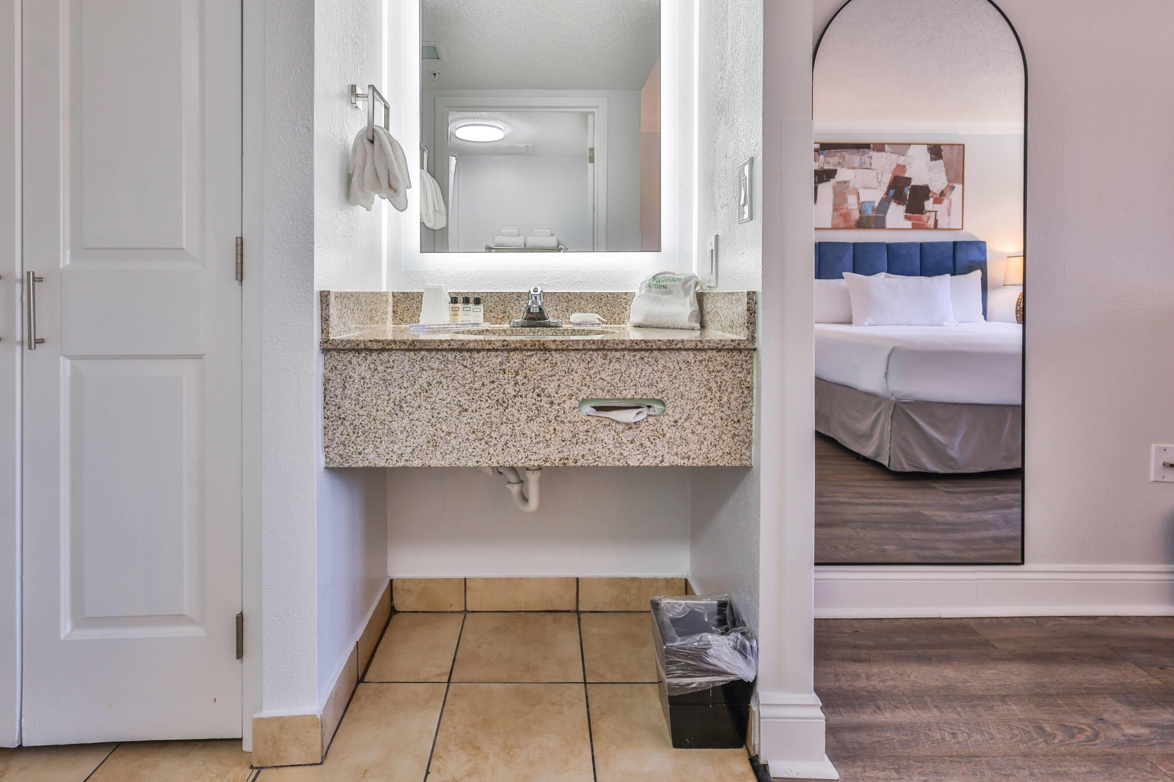 Een hotelbadkamer met een granieten aanrecht, een wastafel, een spiegel en een toilet.