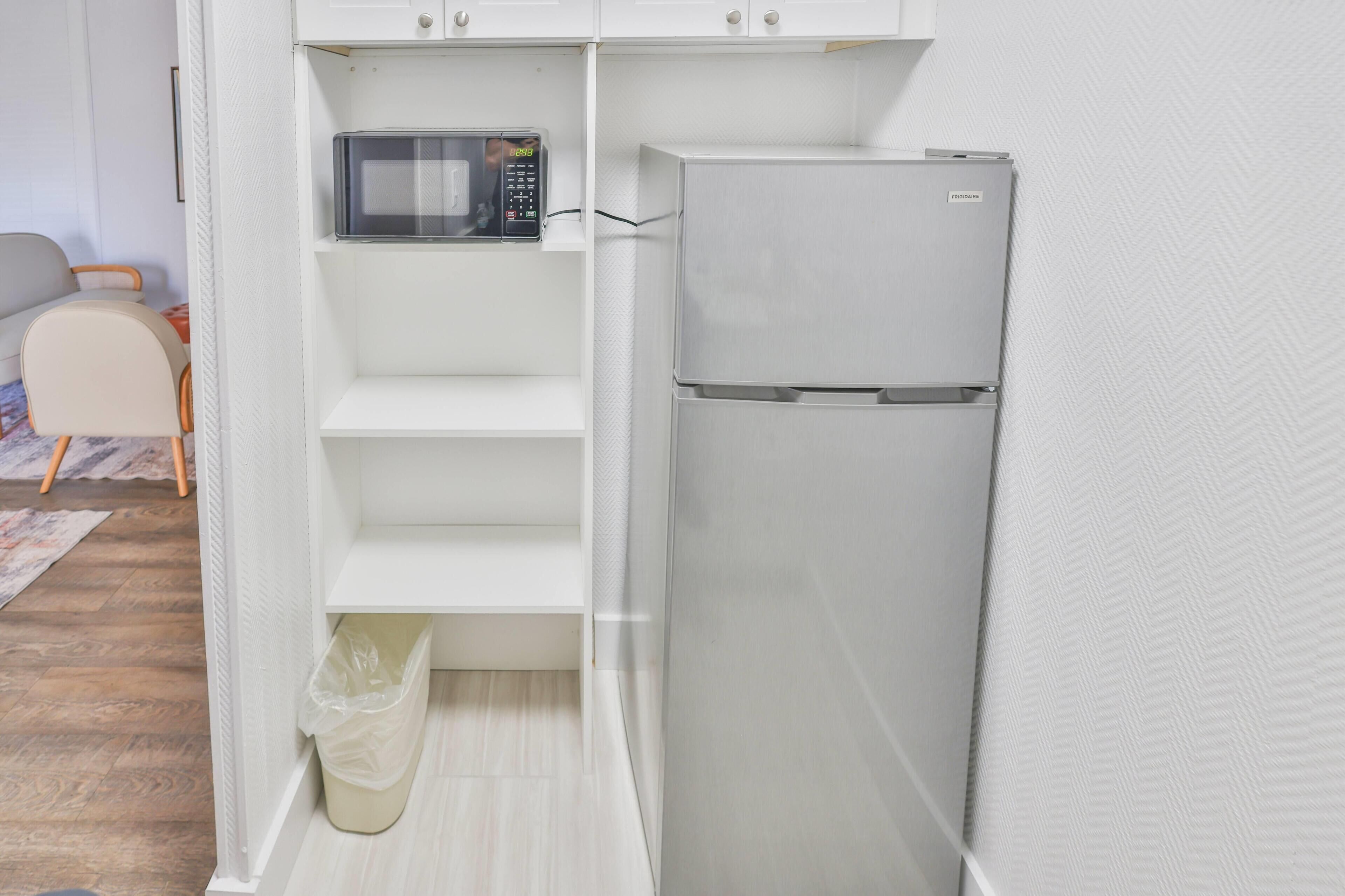 Una cucina compatta con un forno a microonde, un frigorifero e un cestino.