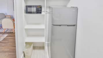 A compact kitchen with a microwave, a refrigerator, and a trash bin.