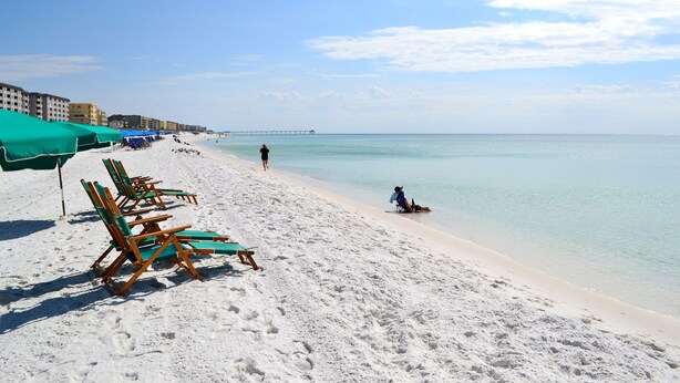 A beach with rows of green umbrellas and wooden lounge chairs.