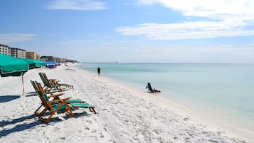 Na praia, areia branca, espreguiçadeiras, guarda-sóis 