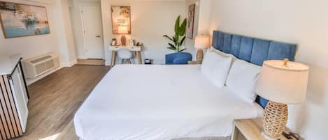 Habitación de hotel con una cama grande, un escritorio, una silla, una planta en maceta y una lámpara.