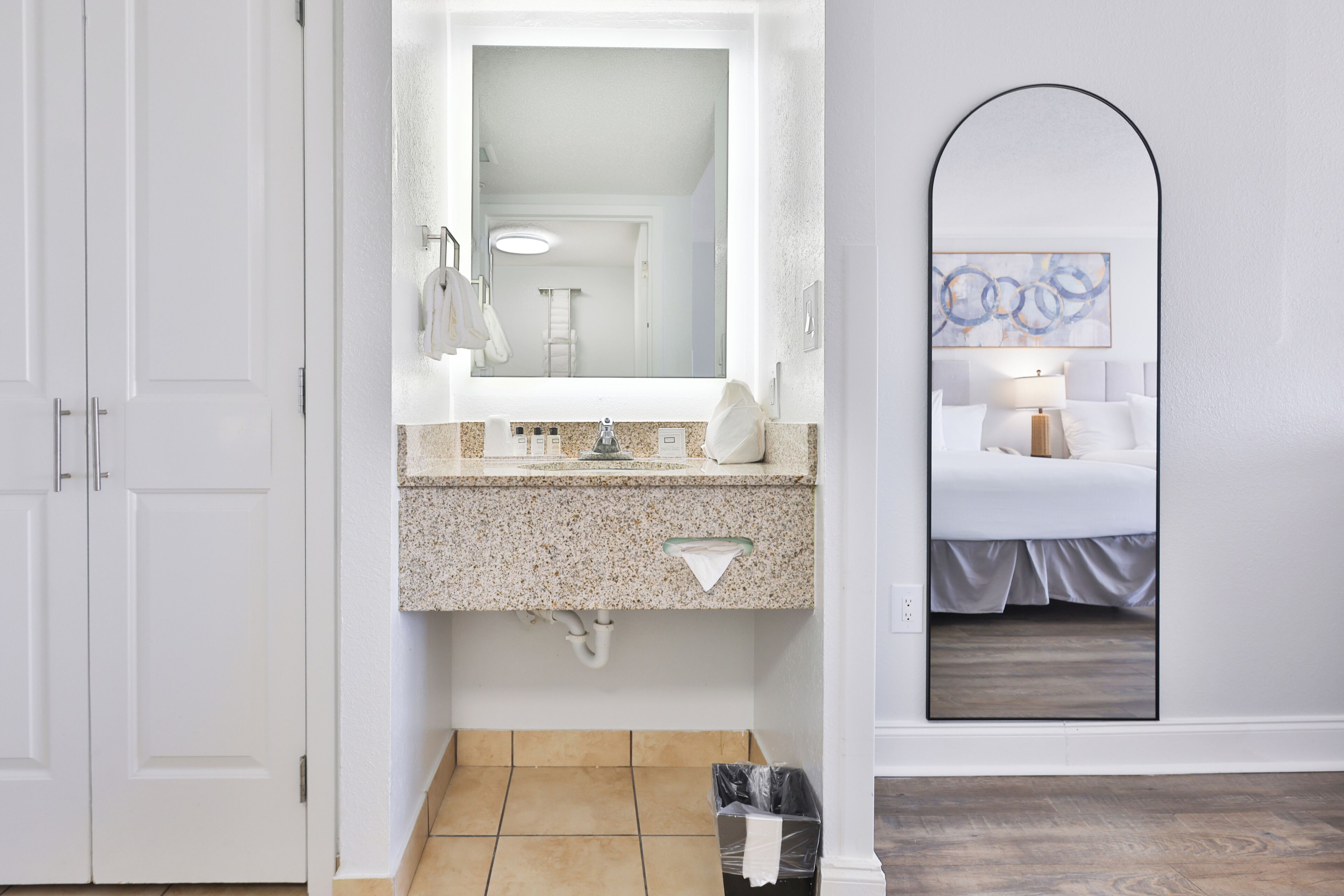 Un bagno con lavandino, specchio e vista su una camera da letto con un letto e un comodino.