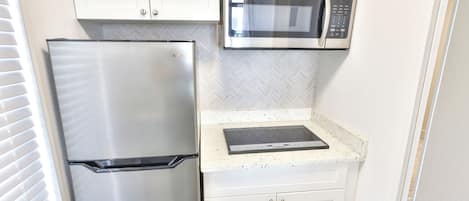 A compact kitchen with a stainless steel refrigerator, a microwave, and a built-in oven.