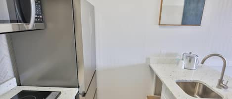 A compact kitchen with a microwave, refrigerator, stove, sink, and a small countertop area.