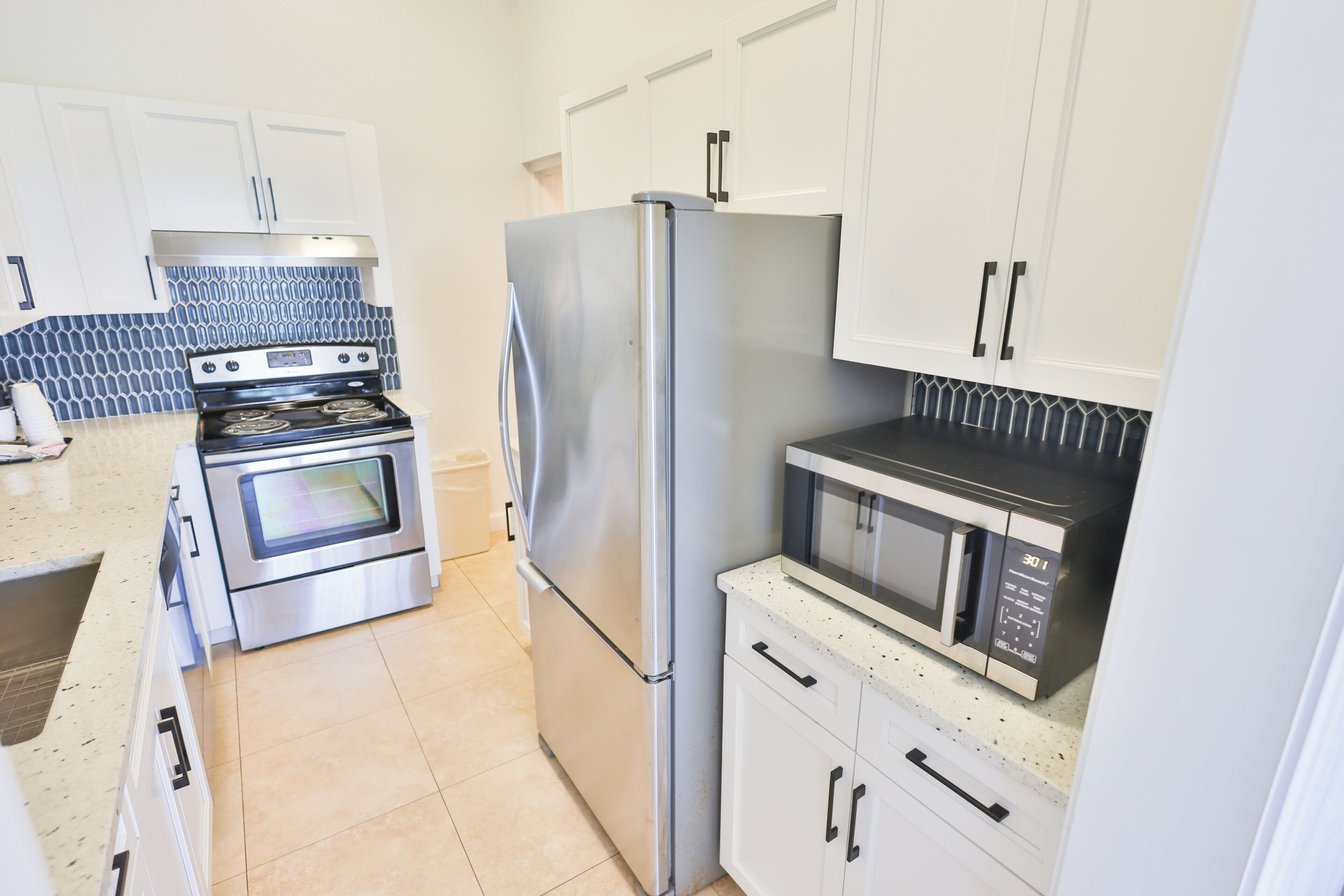 A kitchen with stainless steel appliances, white cabinets, and a patterned backsplash.