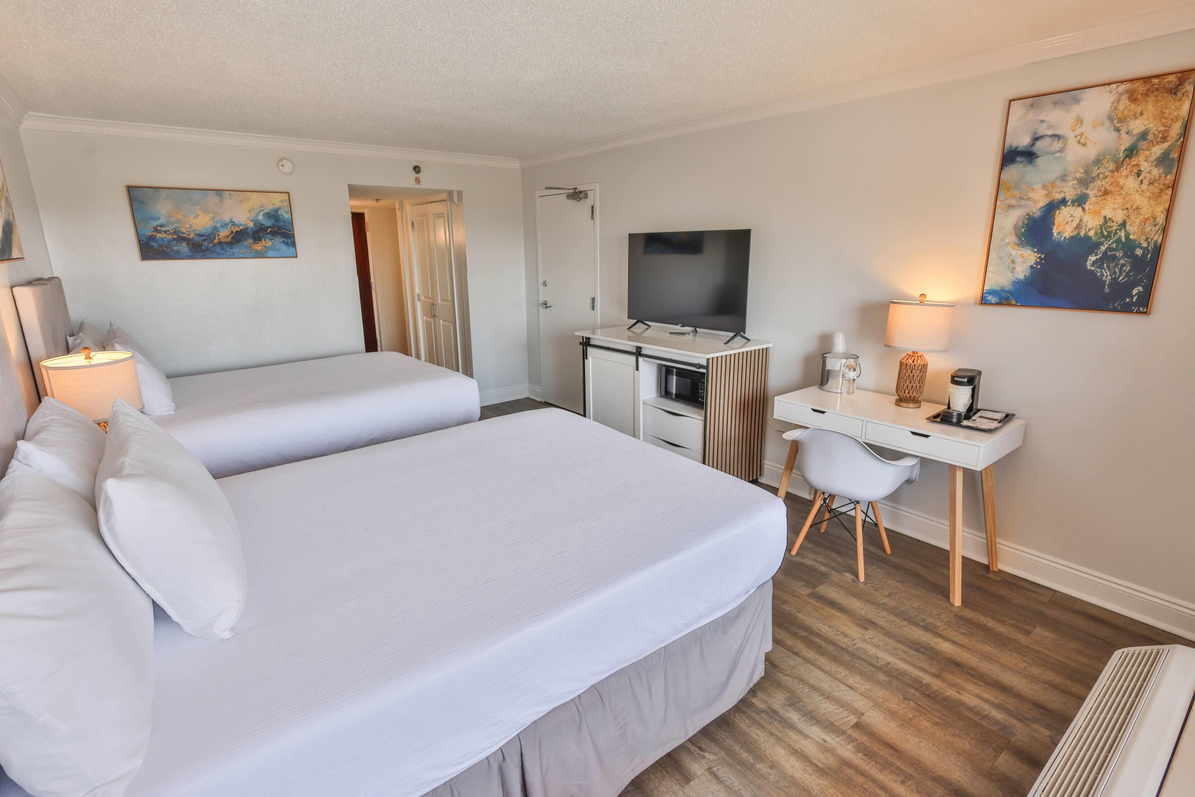 Une chambre d’hôtel avec deux lits, un bureau, une télévision et des œuvres d’art accrochées aux murs.