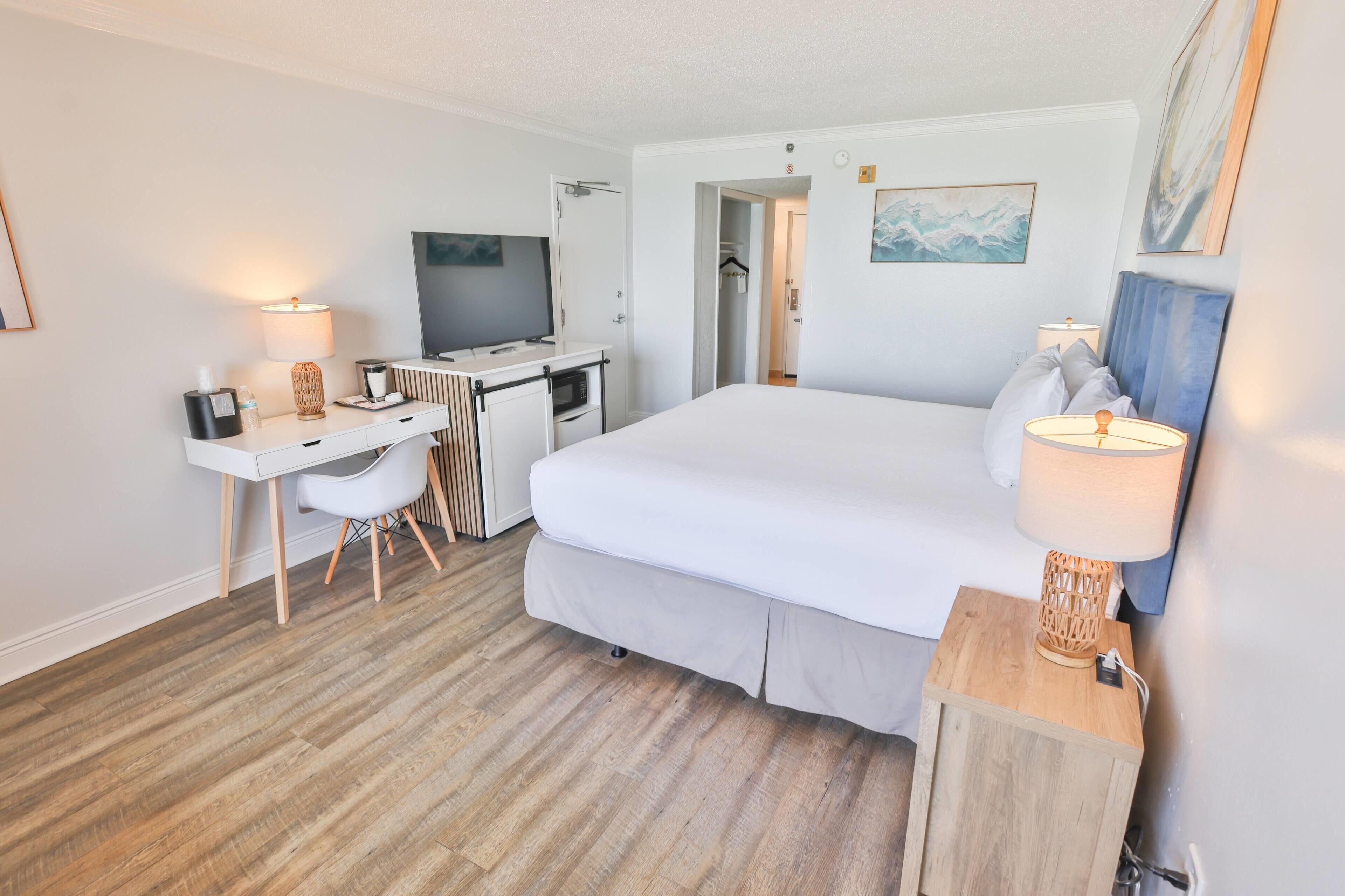 A hotel room with a bed, desk, chair, television, and a lamp.