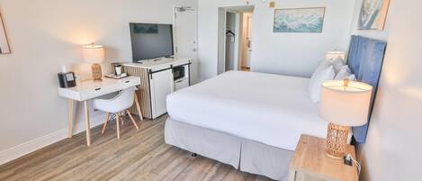 A hotel room with a bed, desk, chair, television, and a lamp.