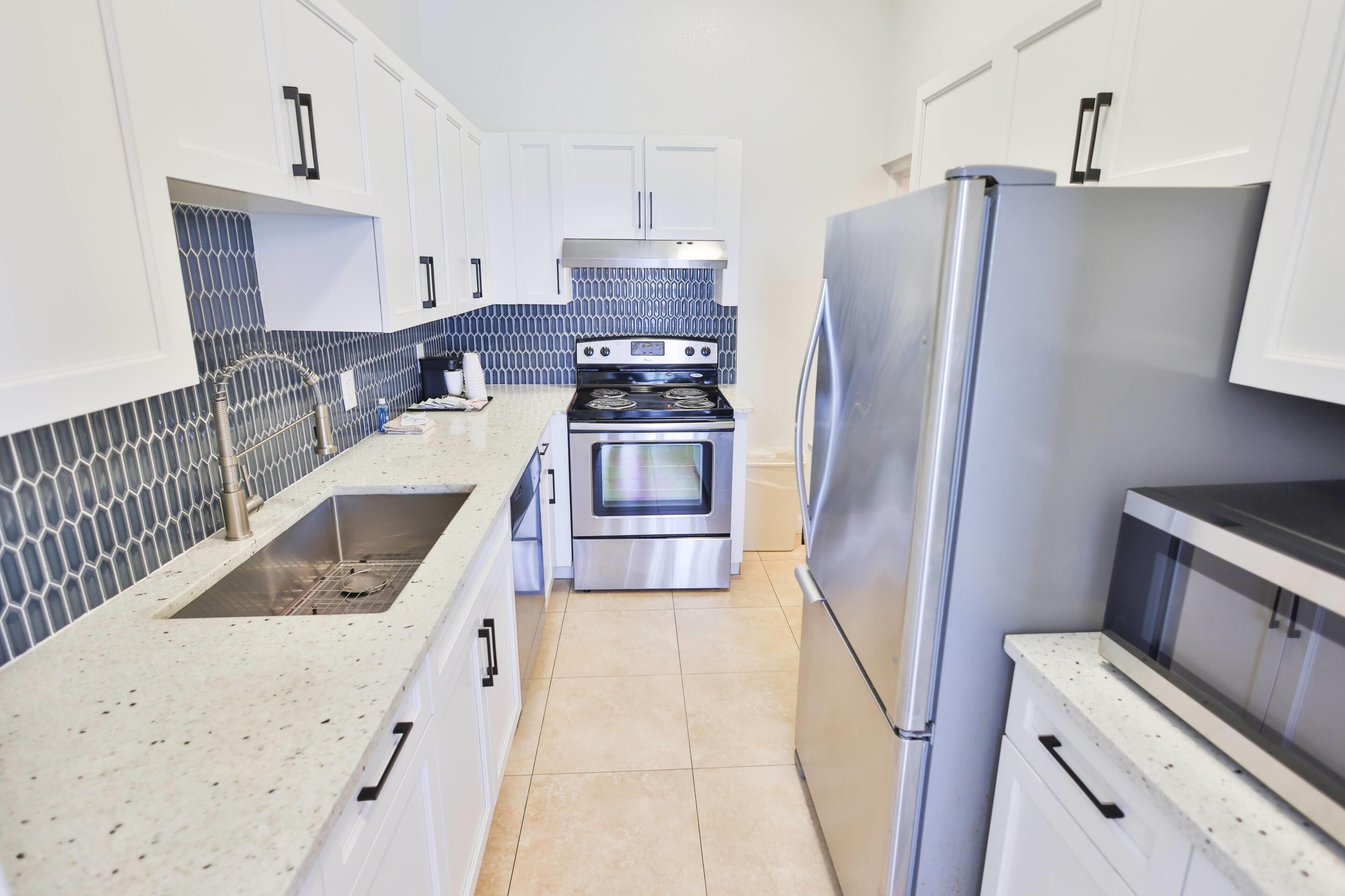 A kitchen with white cabinets, a stainless steel refrigerator, a stove, and a sink.
