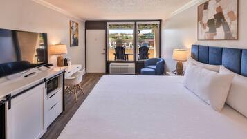 A hotel room with a bed, desk, TV, and a view of the beach through the window.