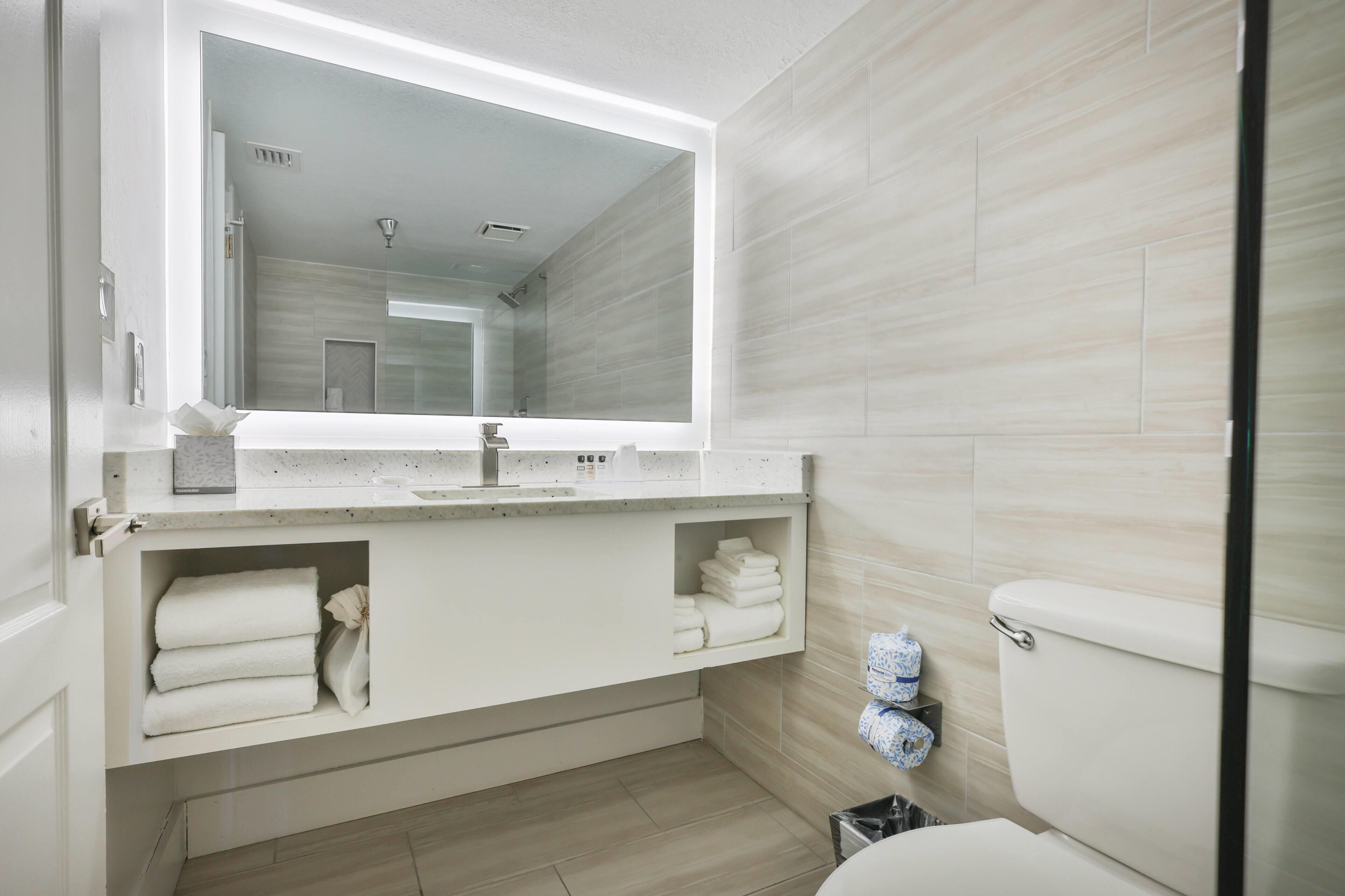 A modern bathroom with a large mirror, a sink, and a toilet.