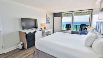 A hotel room with a bed, desk, TV, and balcony with chairs.