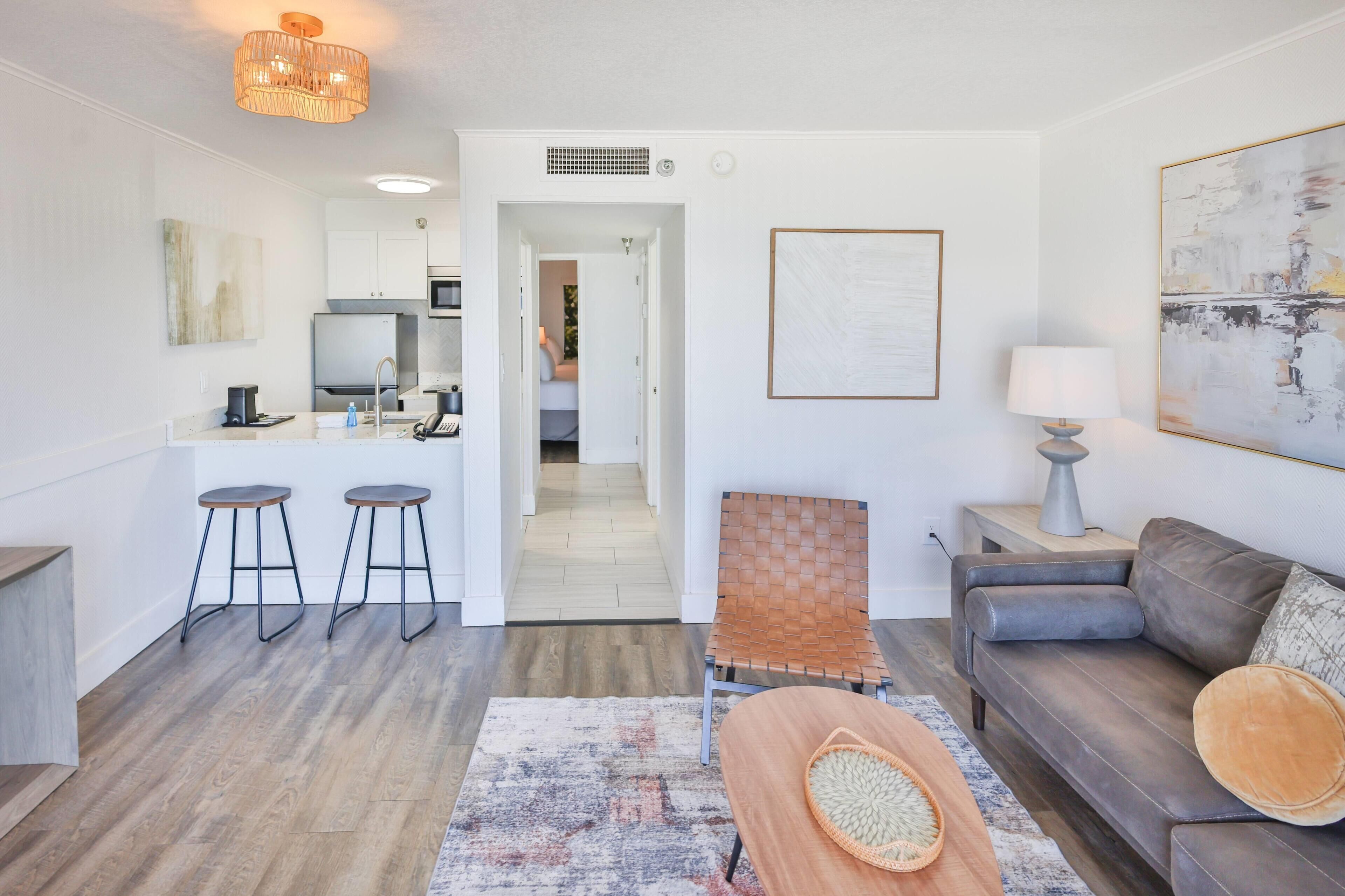 Una sala moderna con sofá, una mesa de centro, una silla y un comedor con taburetes.