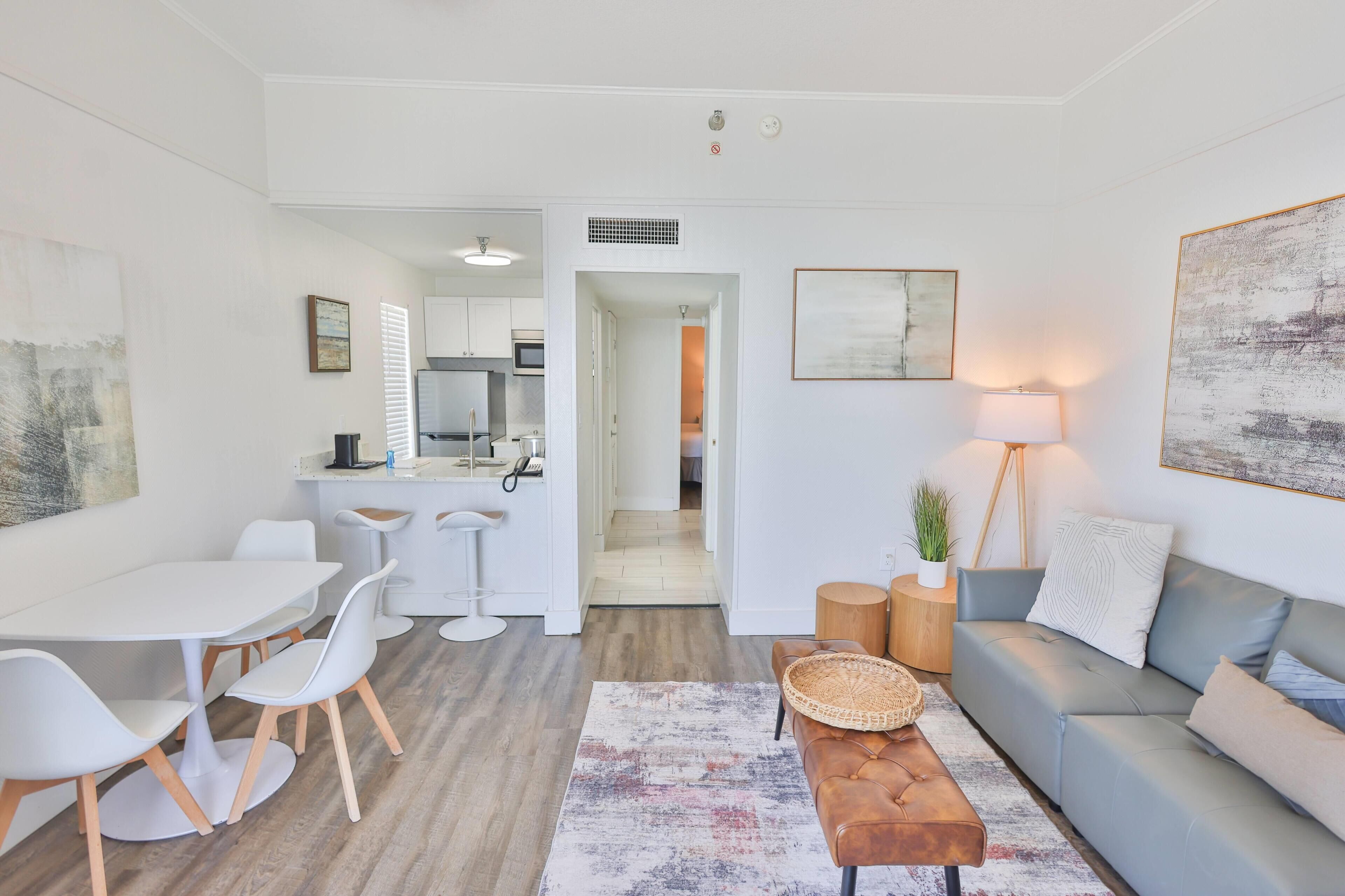 A modern living room with a grey sofa, a coffee table, and a dining area with a white table and chairs.