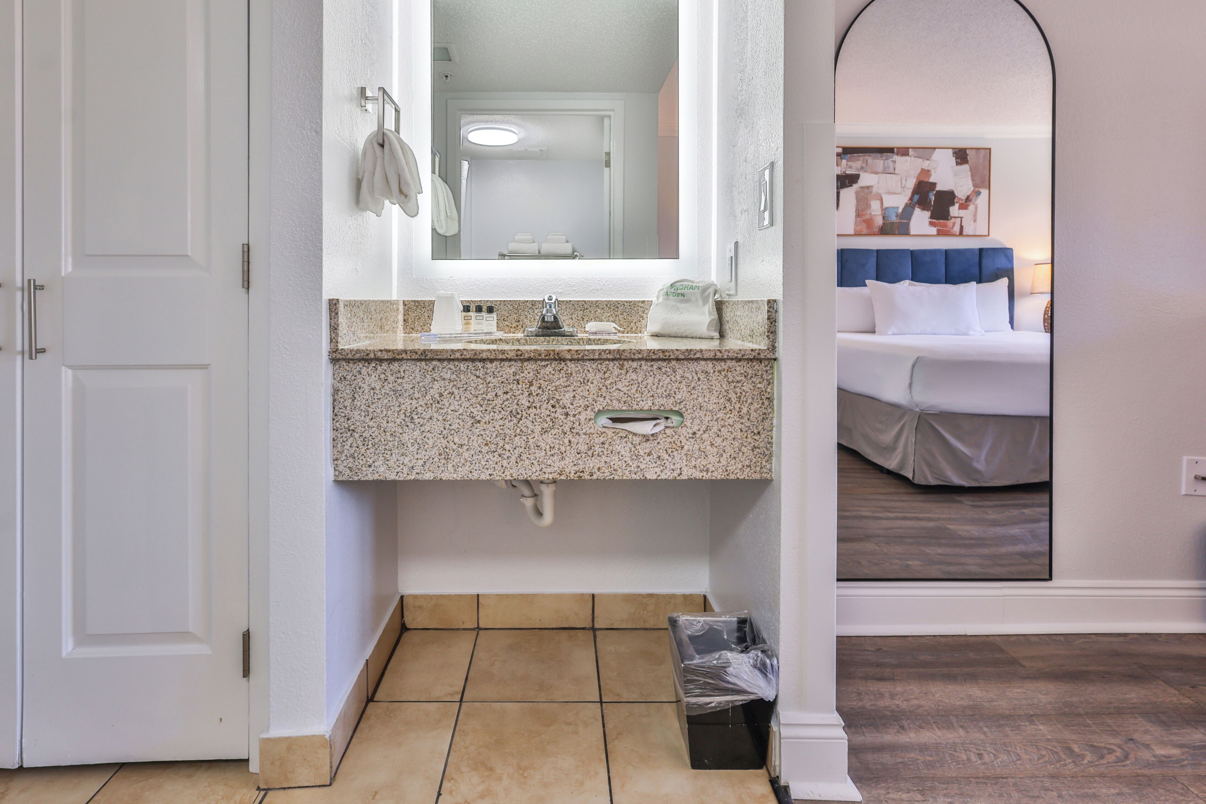 Un baño con encimera de granito, un espejo, un perchero para toallas y un cubo de basura.
