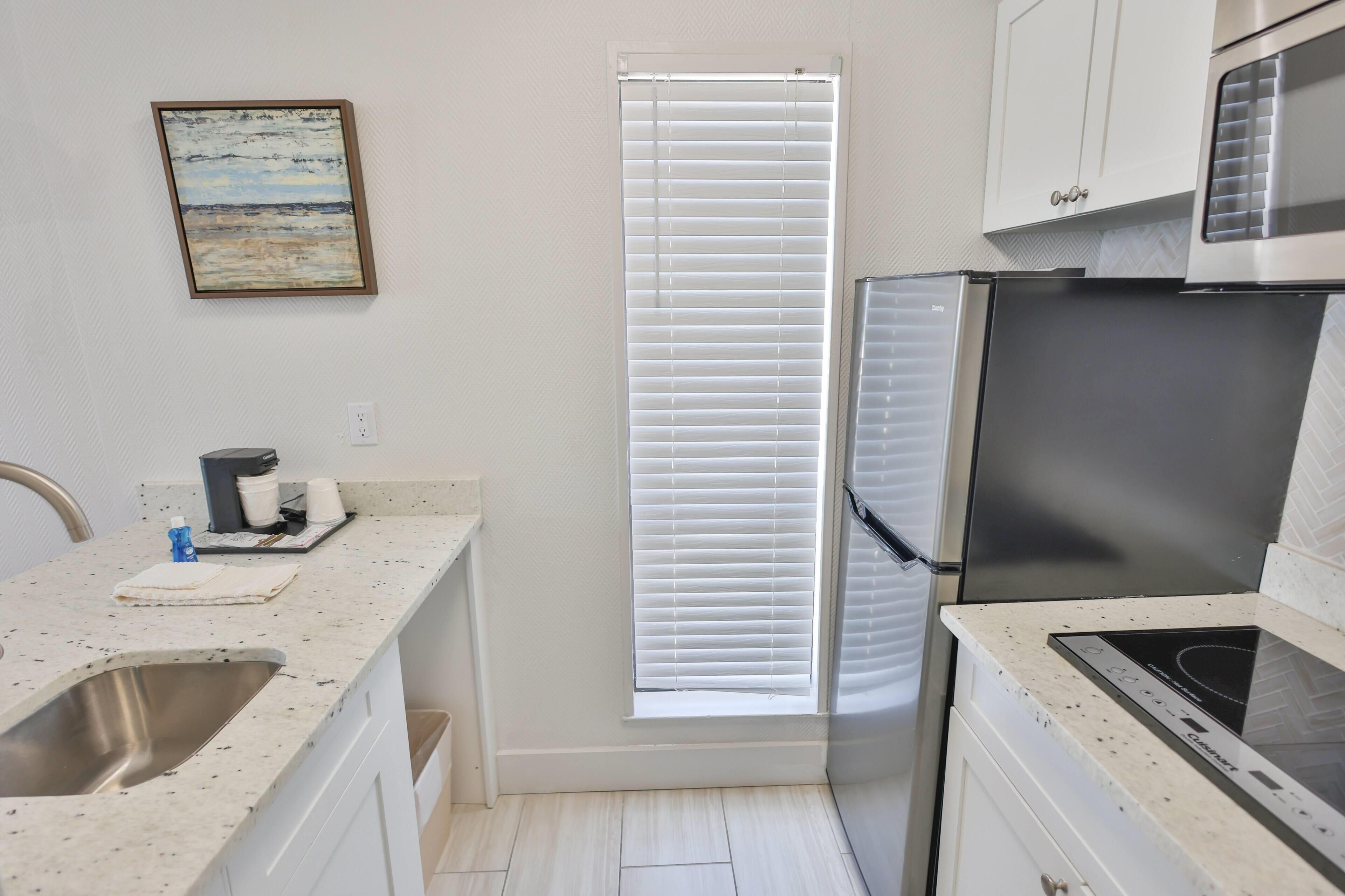 A kitchen with a stainless steel refrigerator, a microwave, a sink, and a window with blinds.