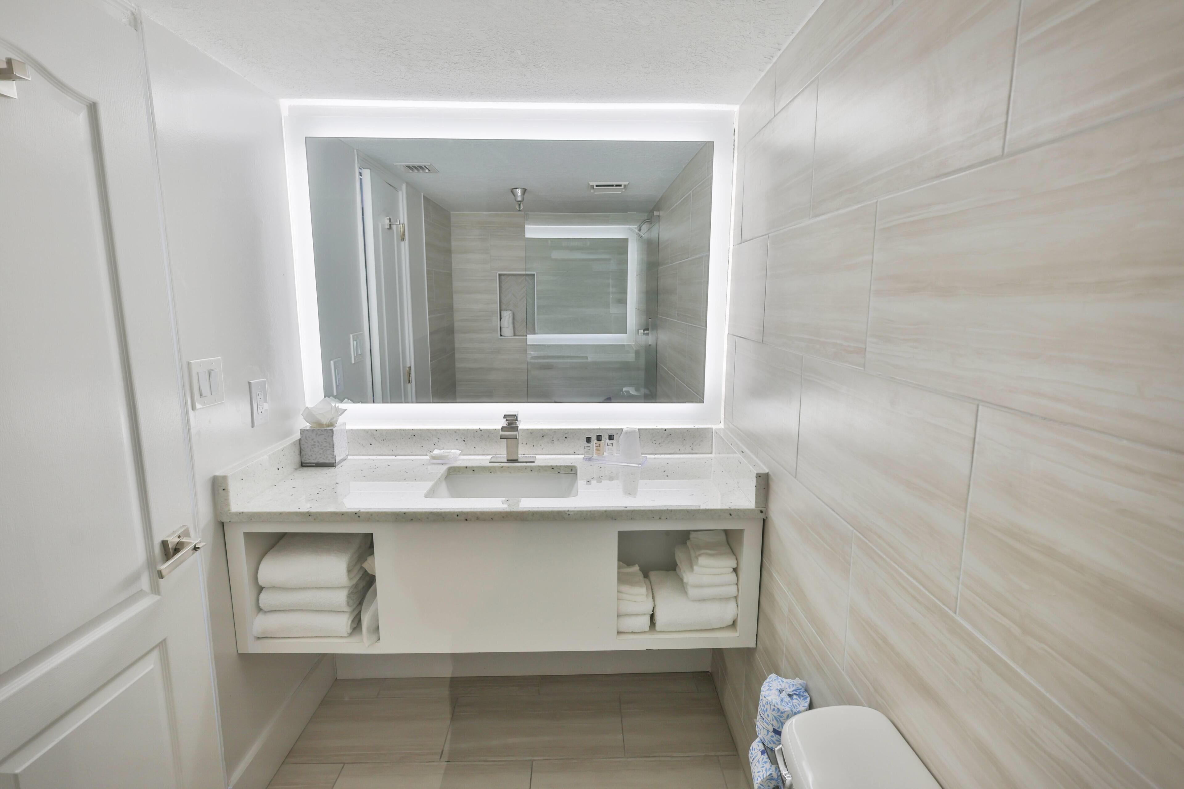 A modern bathroom with a large mirror, white vanity, and a shower area.