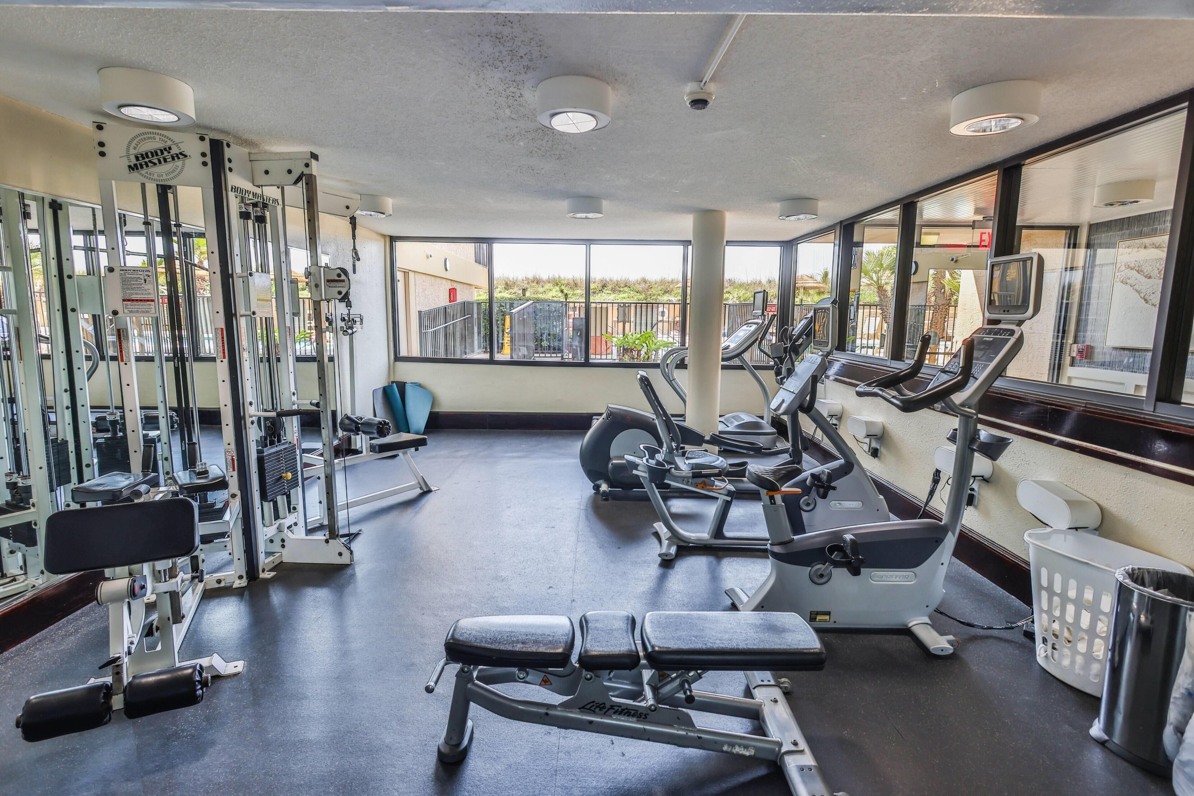 A gym with various exercise equipment, large windows, and a view of the outside.