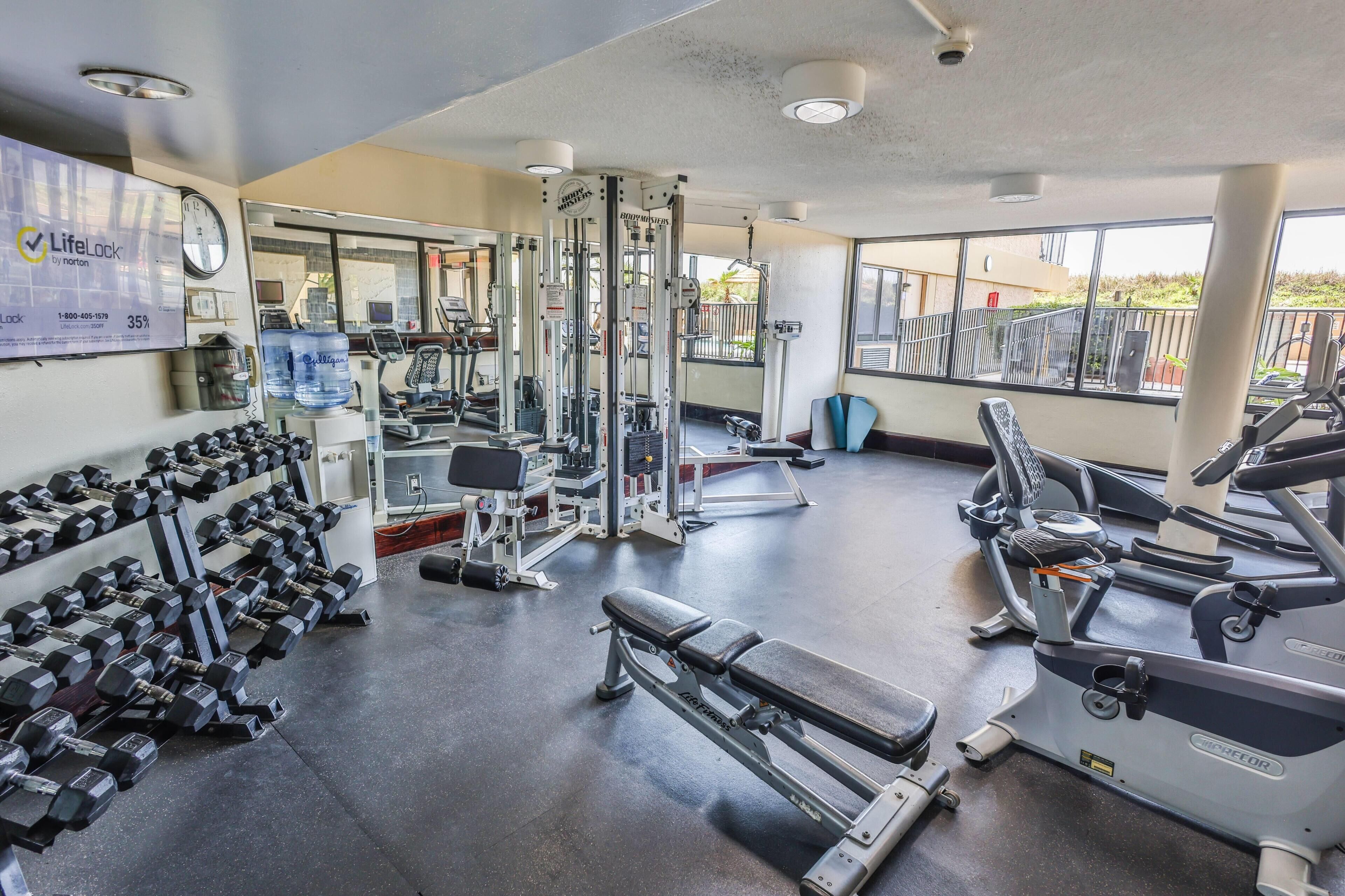 A gym with exercise equipment, dumbbells, and a bench.