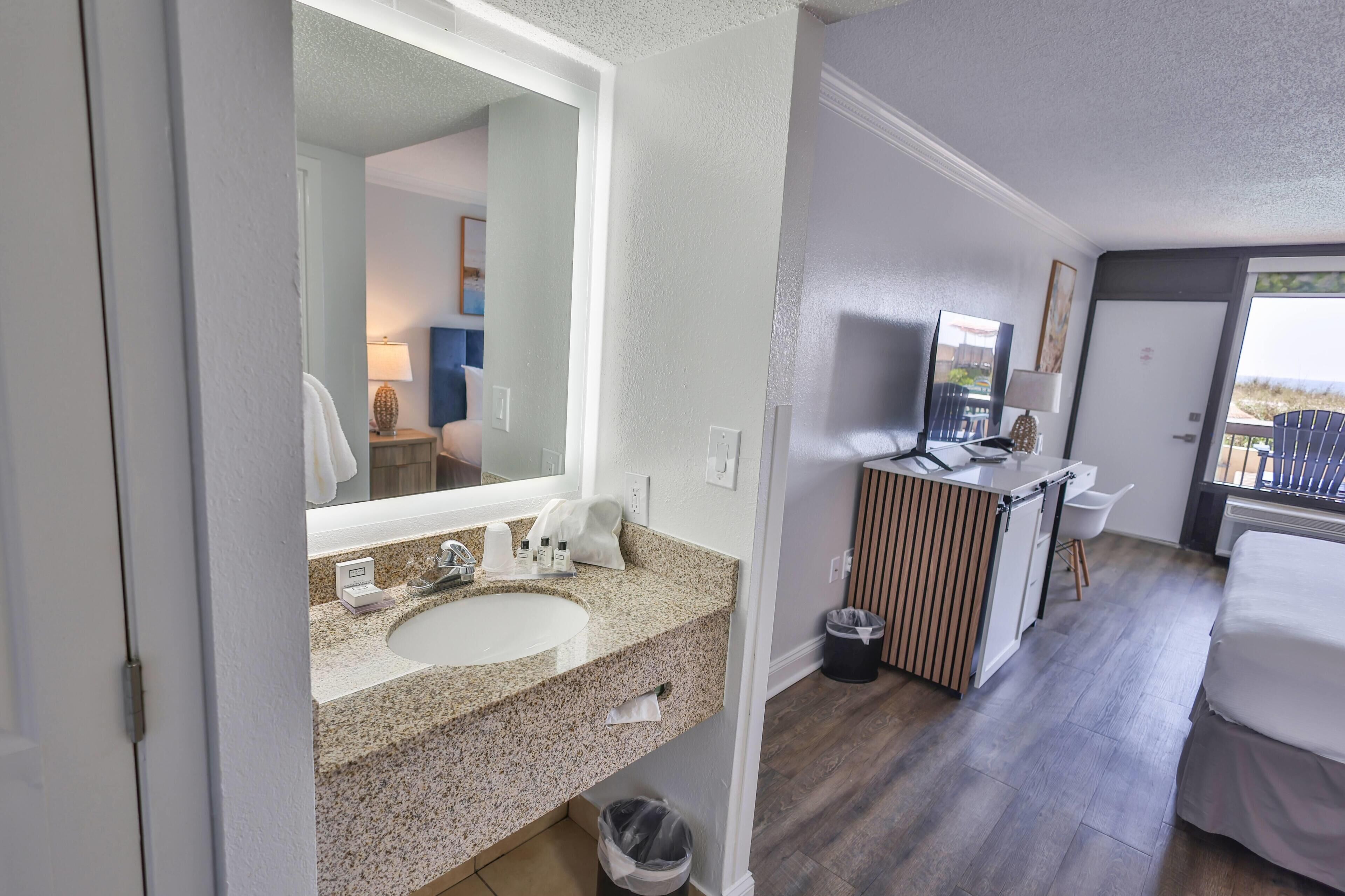 Un bagno d'hotel con lavandino, specchio e un piccolo angolo toilette.