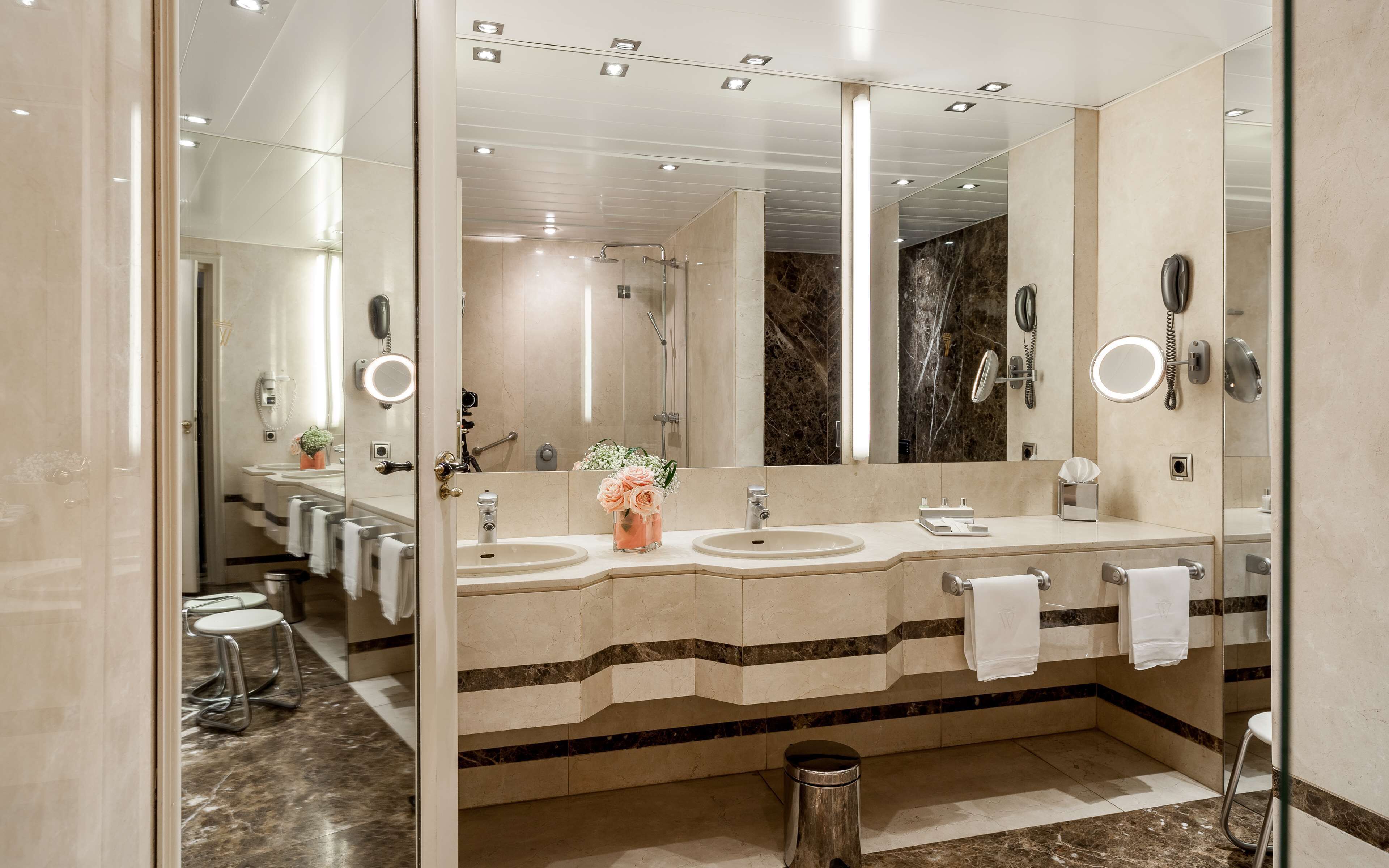 A modern bathroom with three sinks, a large mirror, and a shower.