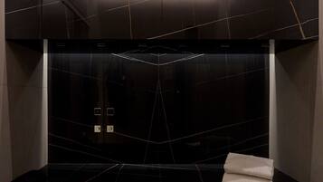 A modern bathroom with black marble tiles, a central light fixture, and a towel rack with folded towels.