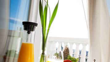A breakfast table with a glass of orange juice, a glass of orange juice, a cup, a plate, a knife, a spoon, a pitcher, a basket of croissants, and a vase with a flower.