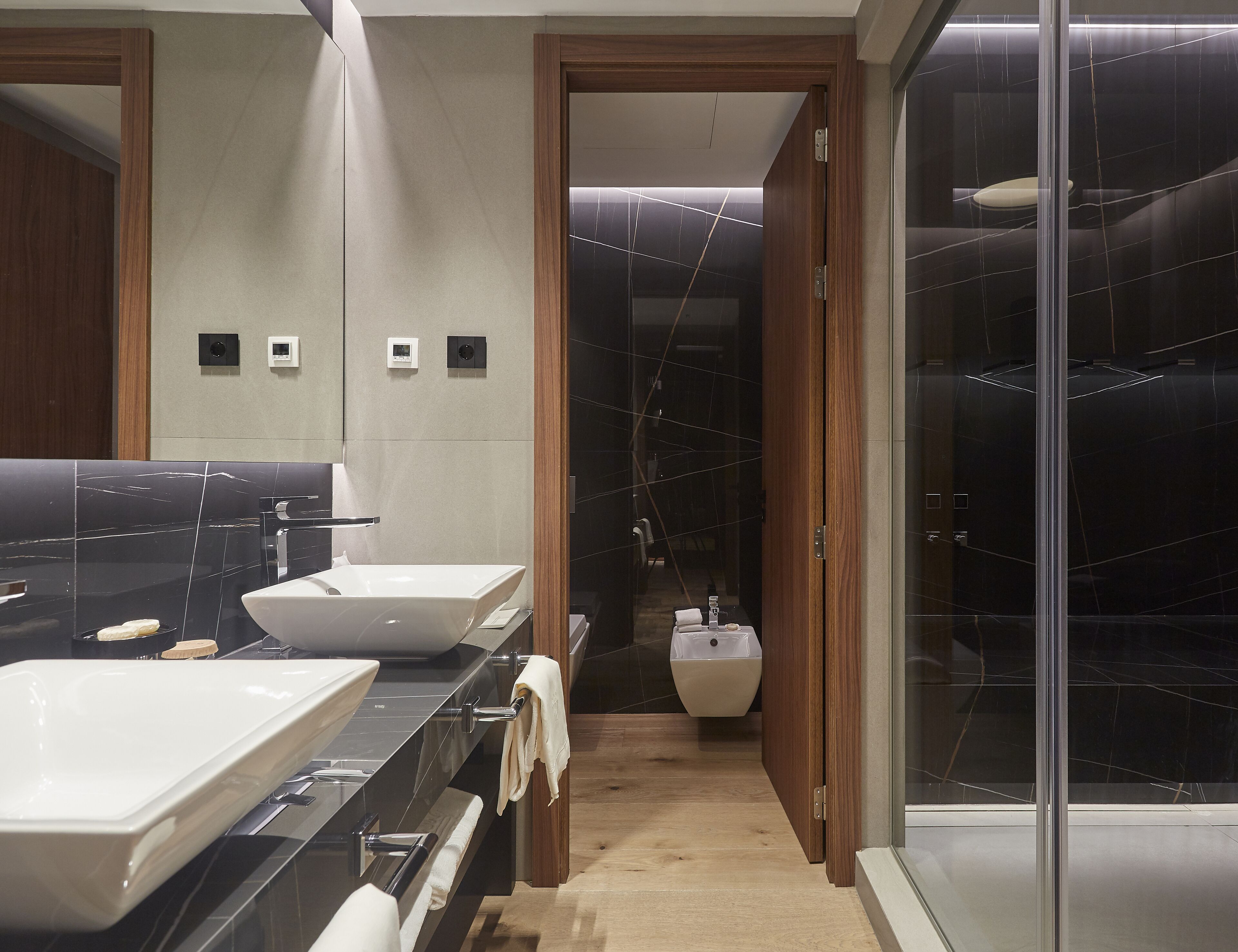 A modern bathroom with a large mirror, two sinks, and a shower area.