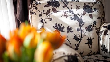 Un sofá con estampado floral y un jarrón con flores naranjas al frente.