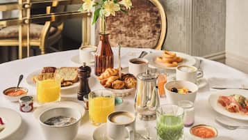 A breakfast table with various dishes, drinks, and a vase of flowers.