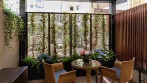 Un balcón con sillas de mimbre, una mesa de vidrio y una planta en maceta con flores.