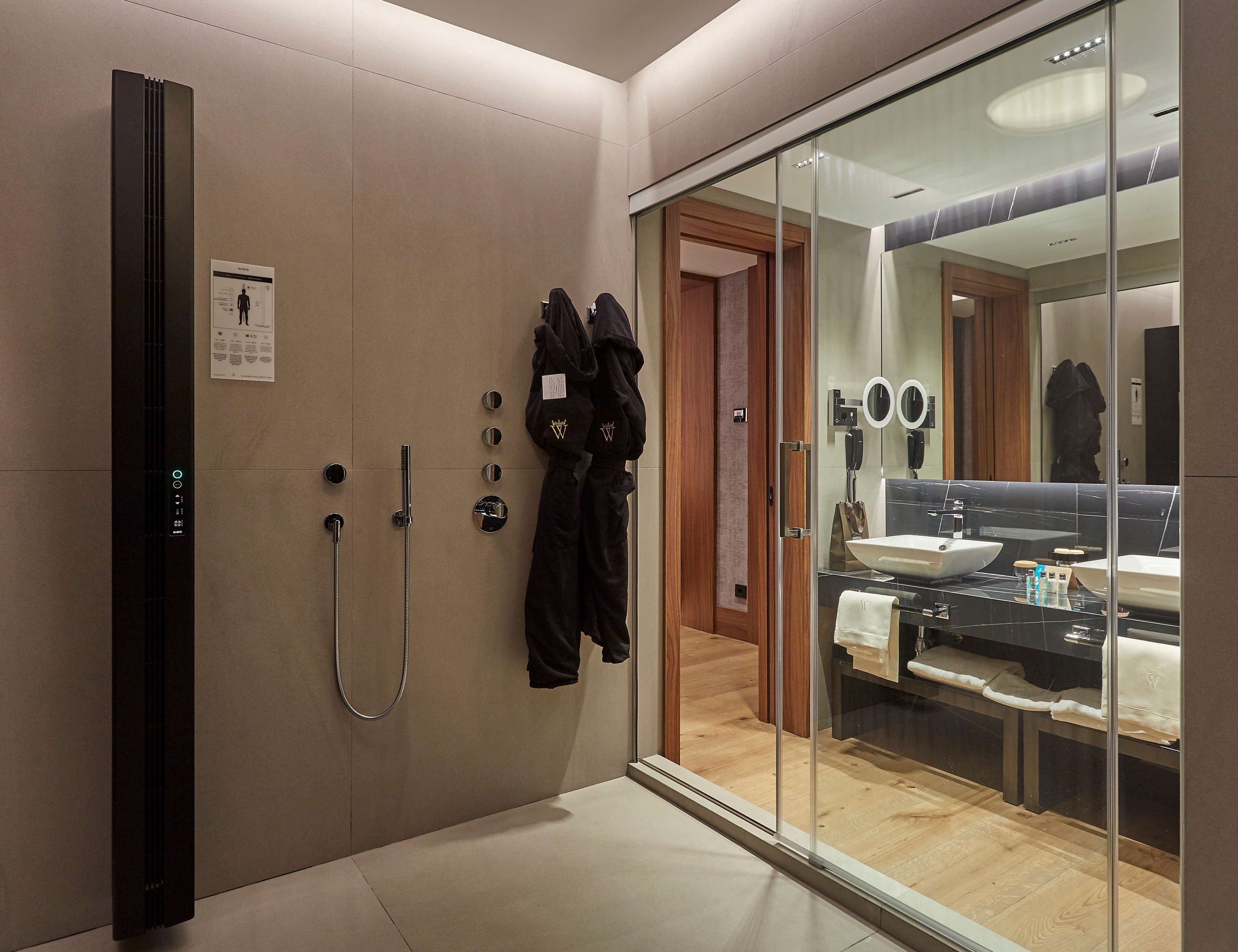 Un baño moderno con cabina de ducha de vidrio, un espejo grande y un tocador con lavabo y toallero.
