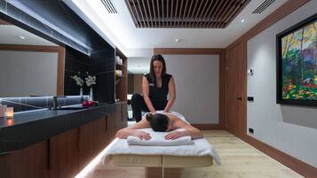 A modern spa room with a massage table, a wooden reception desk, and a large painting on the wall.