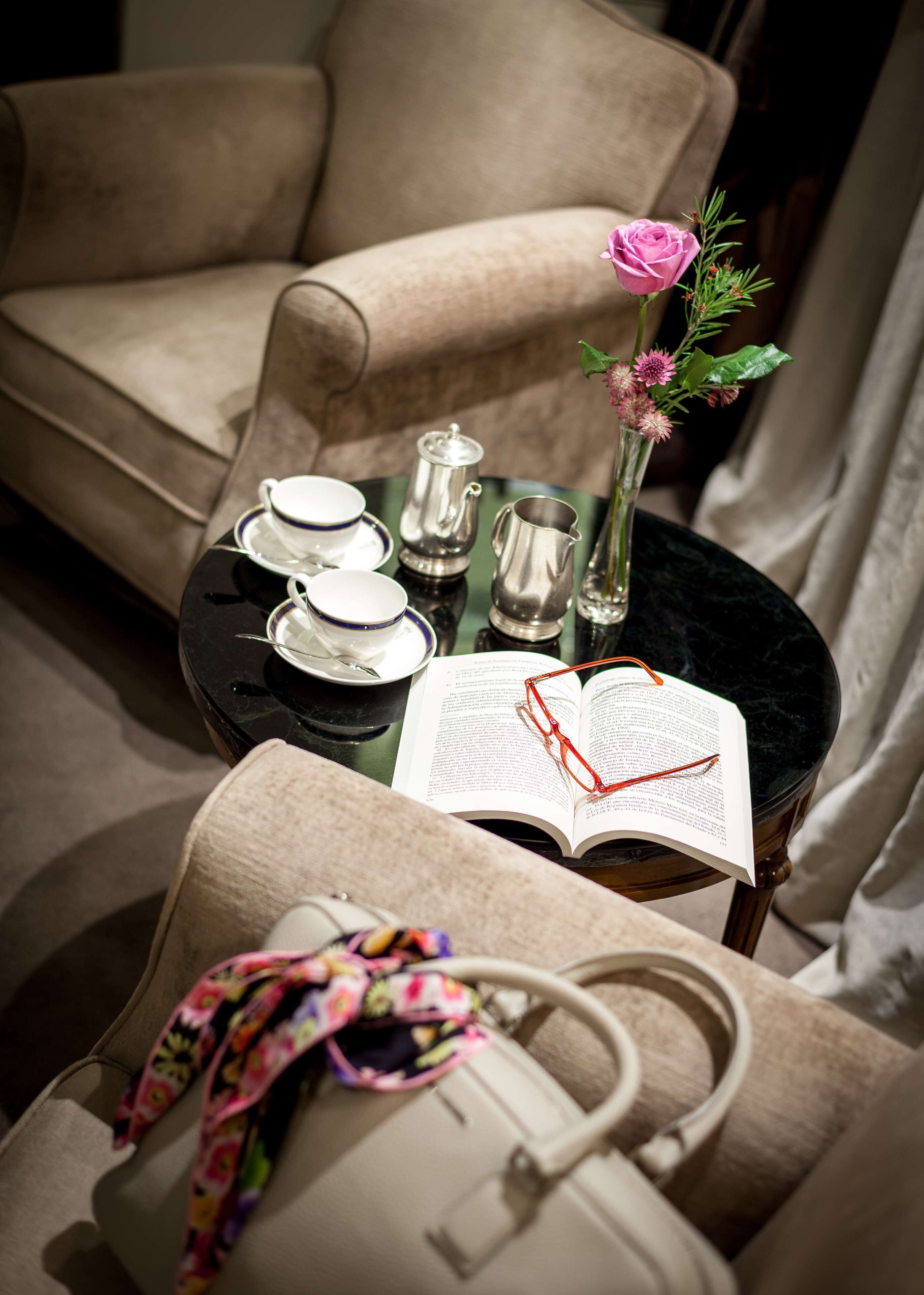 Una habitación acogedora con un sillón color beige, una mesita redonda con un libro, vasos y un bolso.