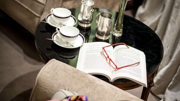 Una habitación acogedora con un sillón color beige, una mesita redonda con un libro, vasos y un bolso.