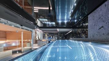 A modern indoor pool area with a glass barrier, ceiling lights, and a textured wall.