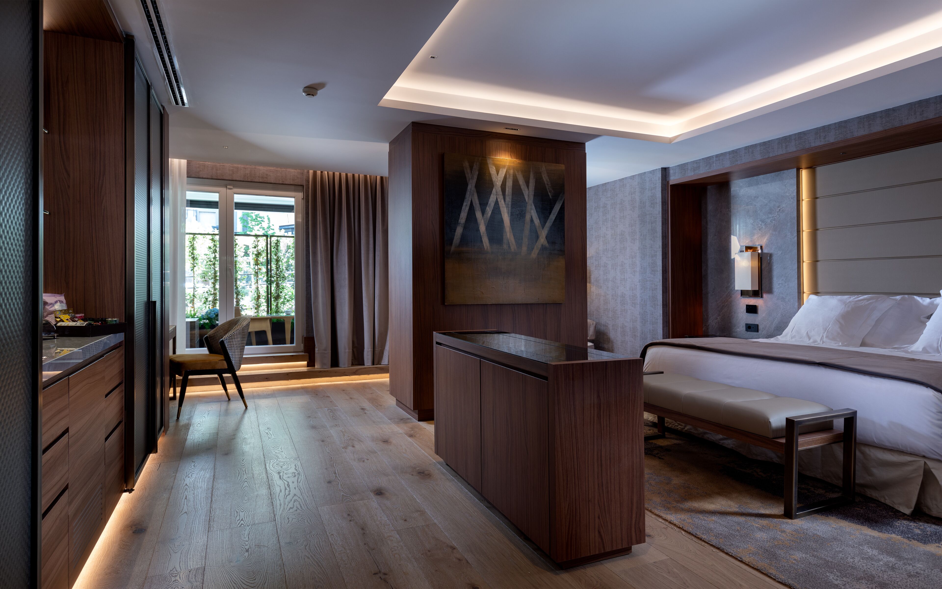 Una habitación de hotel moderna con suelo de madera, un escritorio, una cama y un ventanal con cortinas.