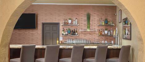 A bar area with a wooden wall, shelves with bottles, and a flat-screen TV.