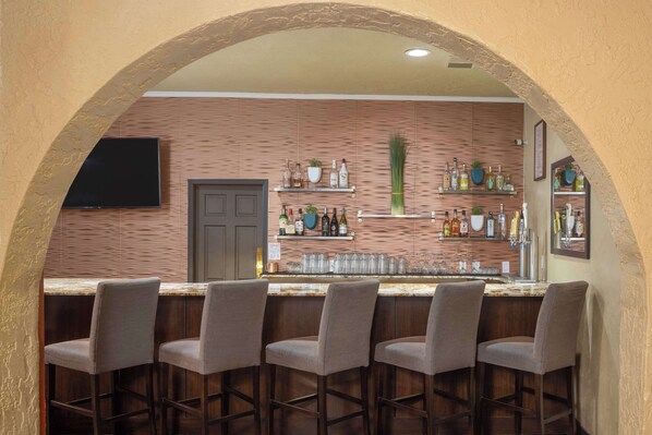 A bar area with a wooden wall, shelves with bottles, and a flat-screen TV. - DoubleTree Suites by Hilton Tucson - Williams Center (Tucson)