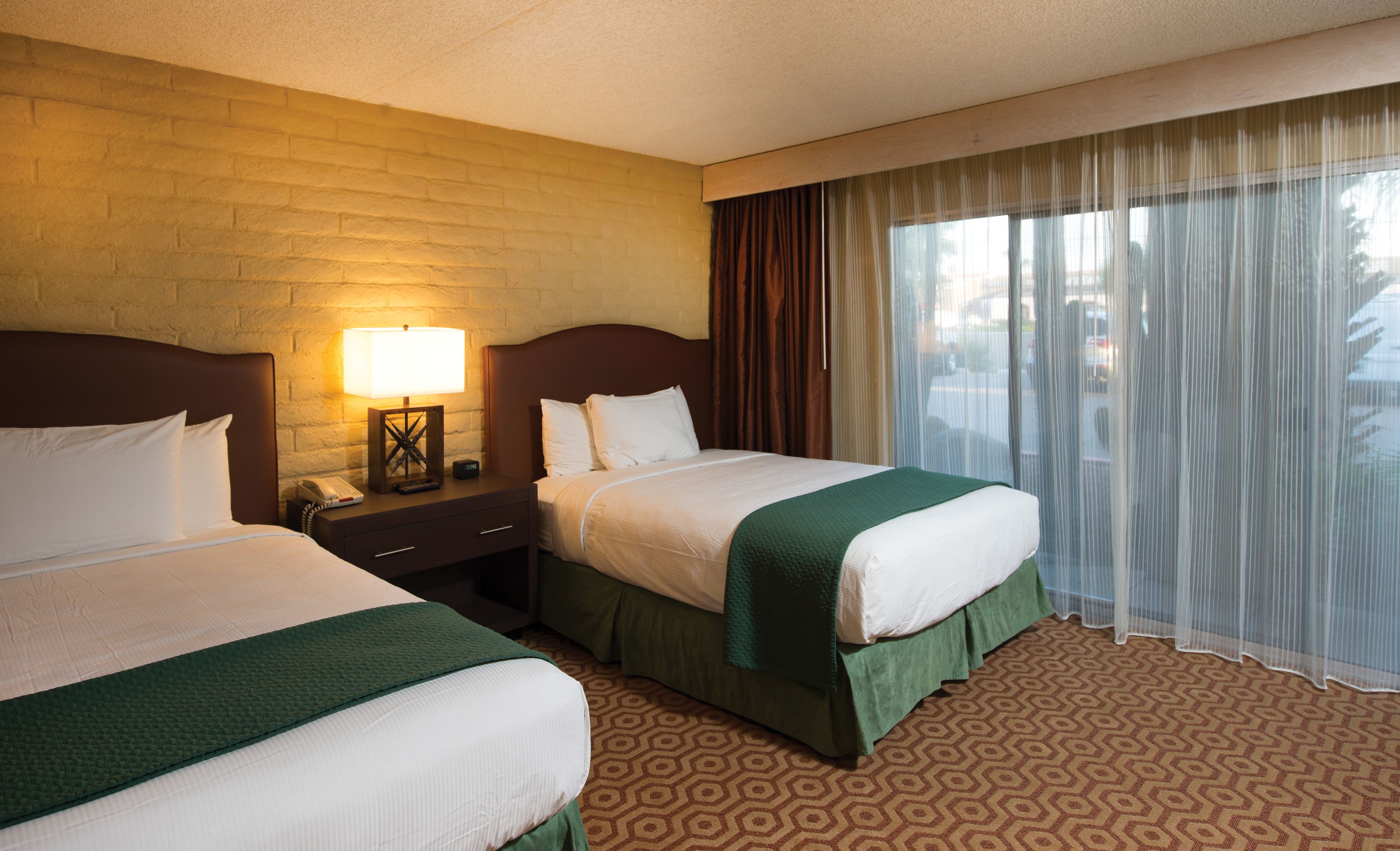 A hotel room with two beds, a nightstand with a lamp, a telephone, and a window with curtains.