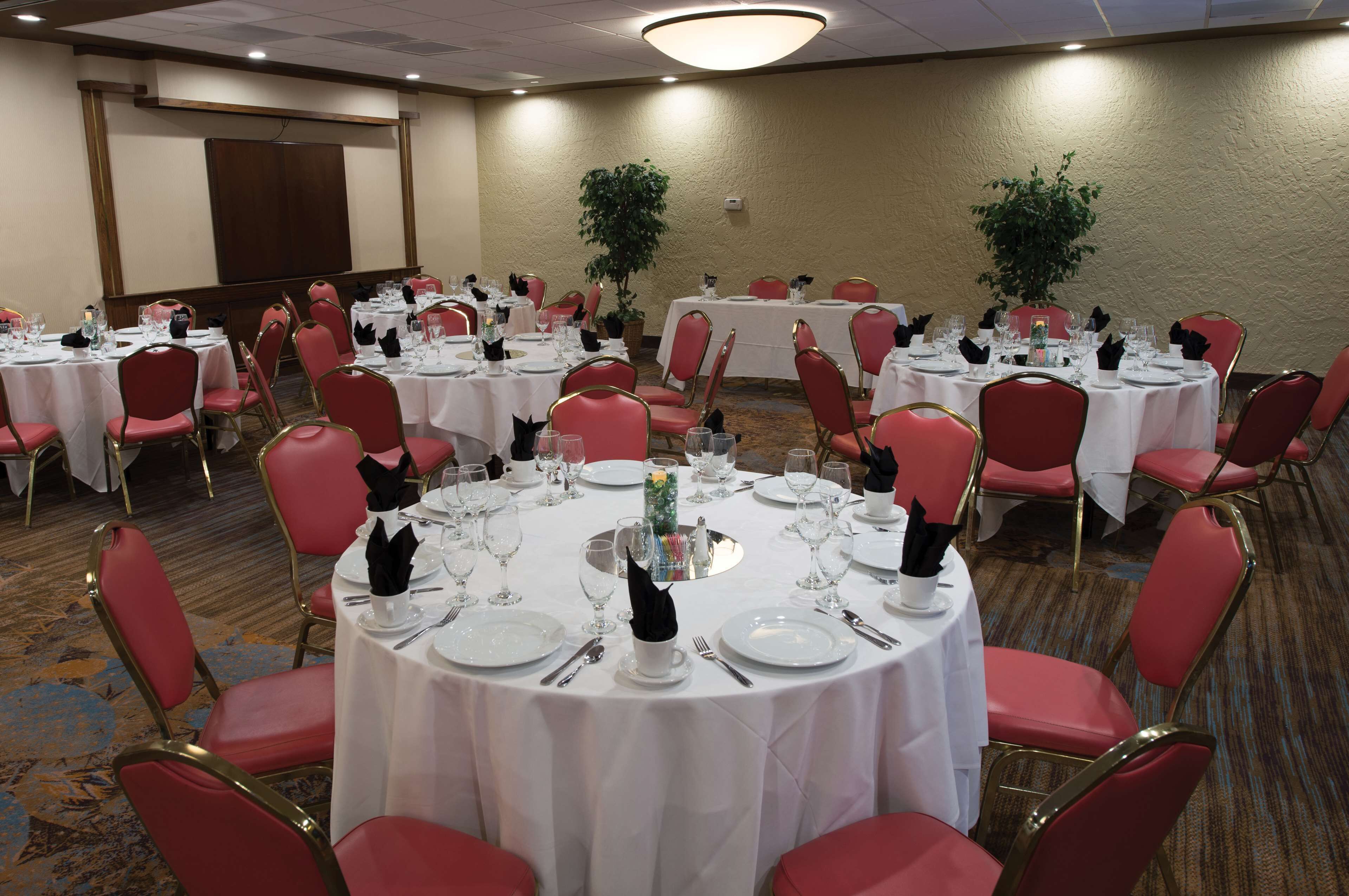 A conference room with round tables, red chairs, and white tablecloths.