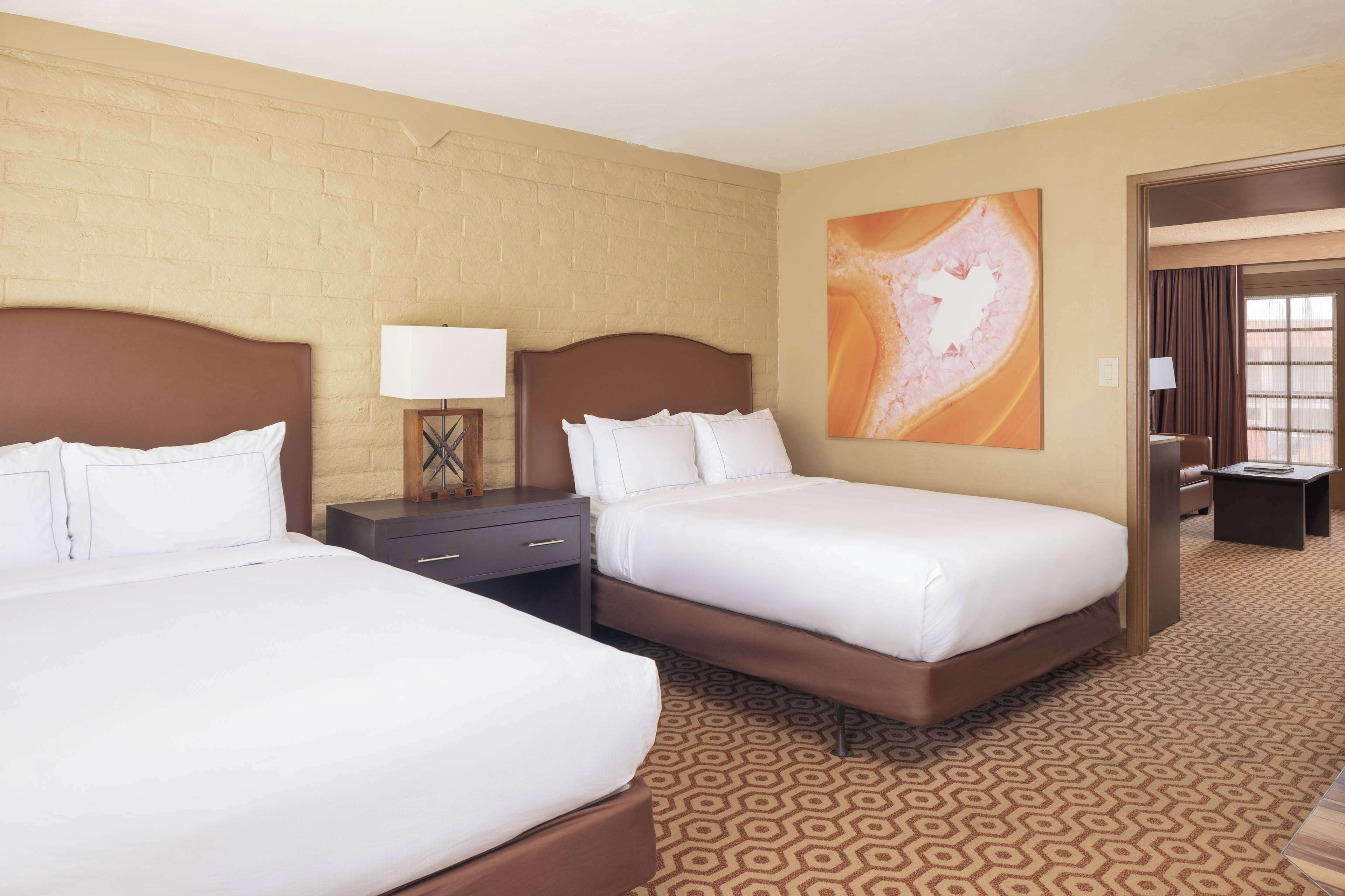 A hotel room with two beds, a brick wall, a large abstract painting, and a patterned carpet.