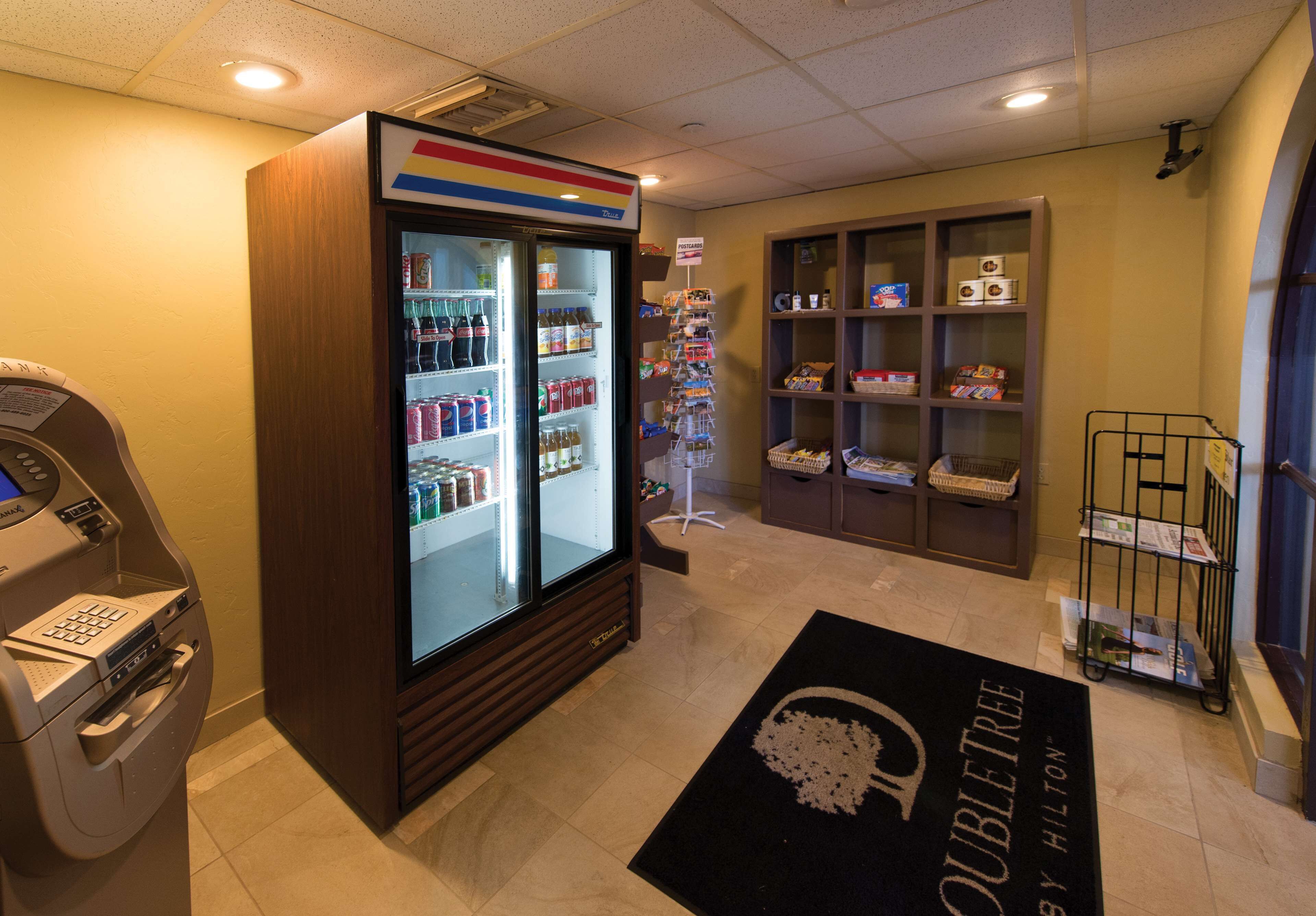 A hotel lobby with a self-service kiosk, a minibar, a display of toiletries, and a reception desk.