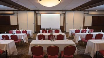Un salón de conferencias con varias mesas y sillas rojas, una pantalla de proyector y una lámpara de araña grande.
