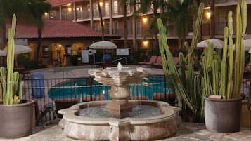 Un patio con una fuente de piedra, una piscina y cactus en macetas.