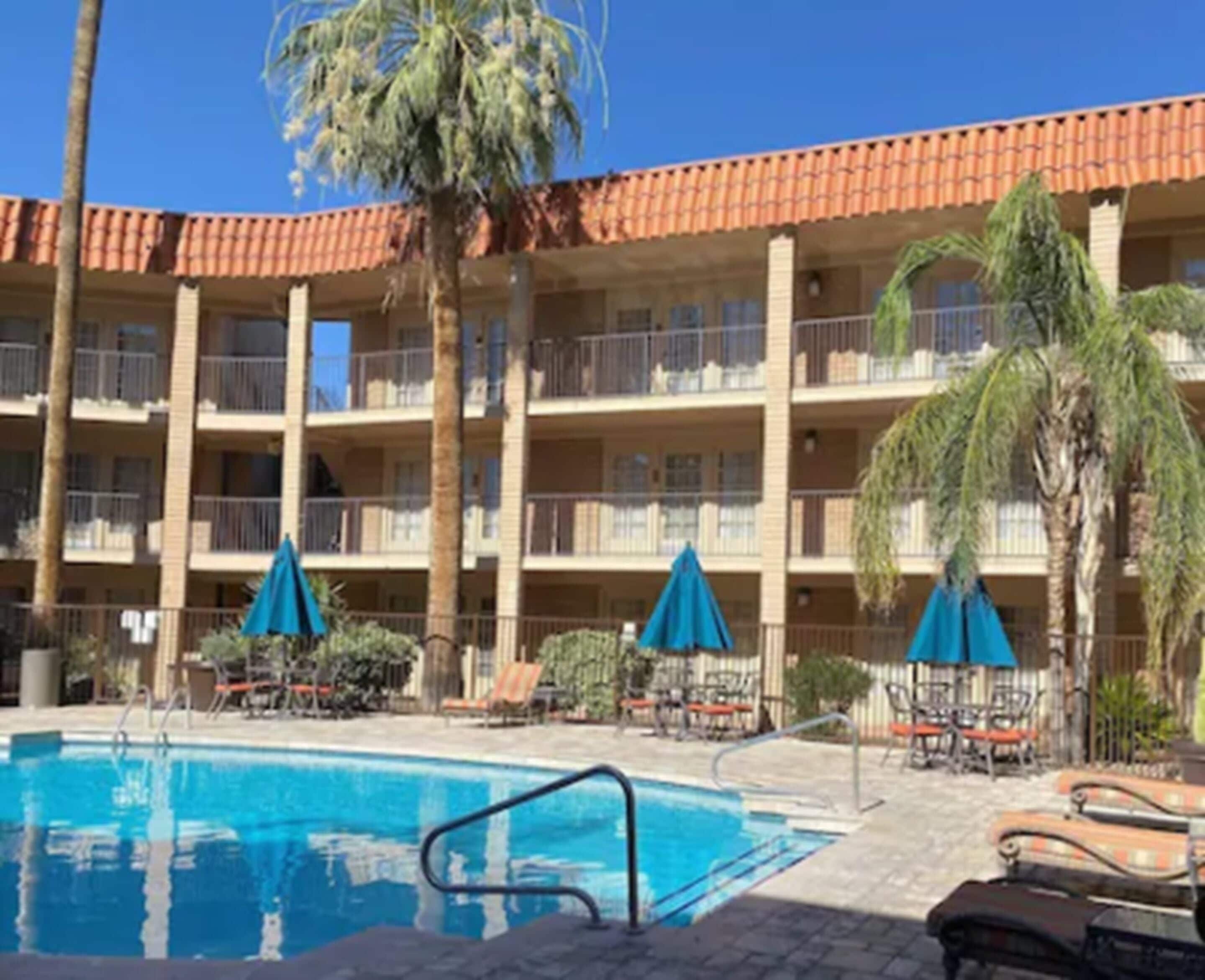 A hotel with a swimming pool, palm trees, and outdoor seating.