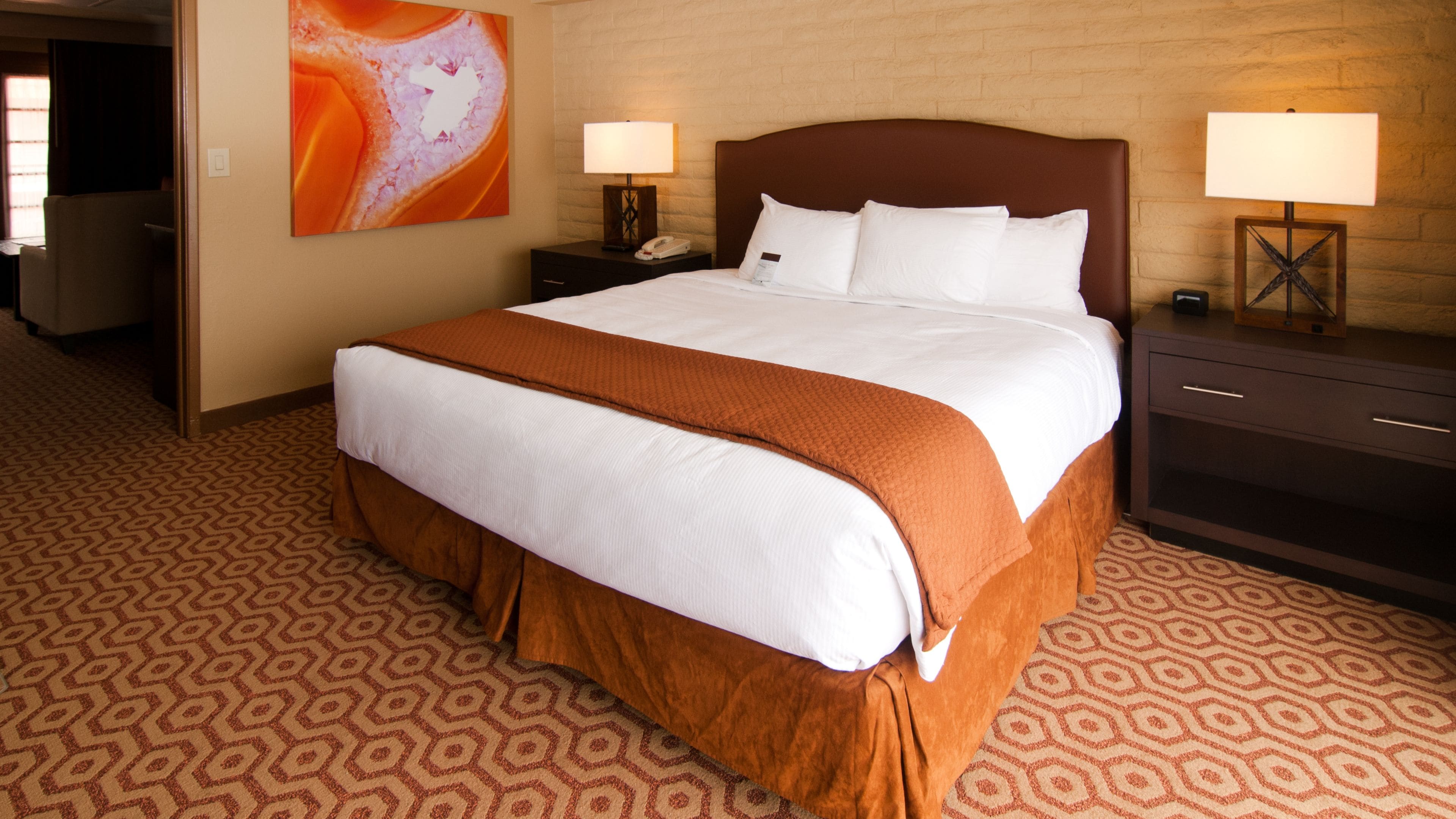 A hotel room with a large bed, two bedside tables with lamps, a wall-mounted phone, and a patterned carpet.
